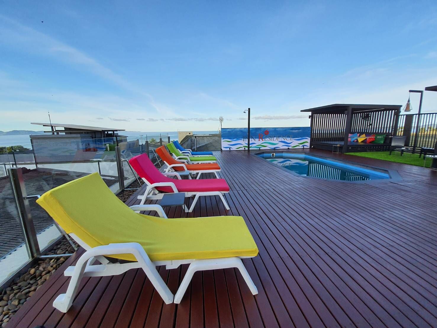 A deck with colorful lounge chairs, a pool, and a view of the ocean.
