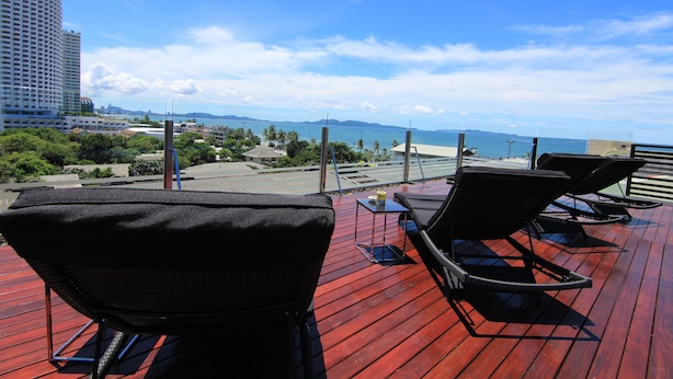 Une terrasse sur le toit, dotée de chaises longues et offrant une vue sur l’océan et le paysage urbain.