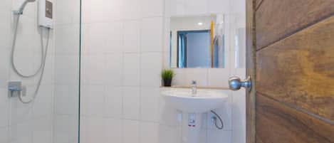 Un baño moderno con cabina de ducha de vidrio, un lavabo blanco y una puerta de madera.