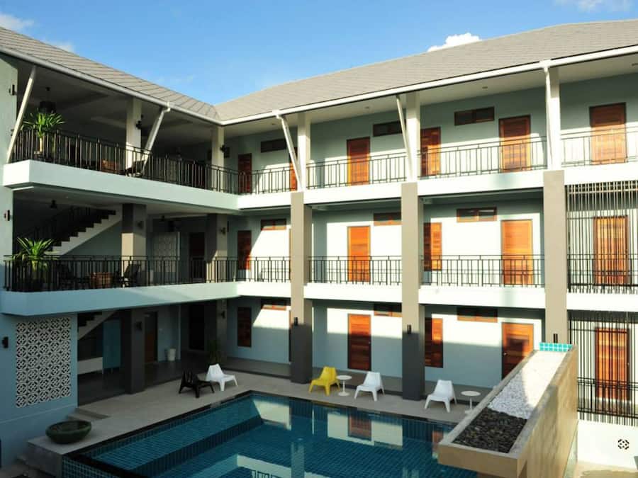 A multi-story hotel with a central courtyard featuring a swimming pool, outdoor seating, and balconies.