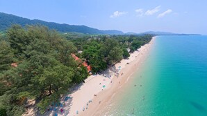 Vista aerea di una spiaggia con acque turchesi cristalline, una spiaggia sabbiosa e vegetazione lussureggiante a sinistra.