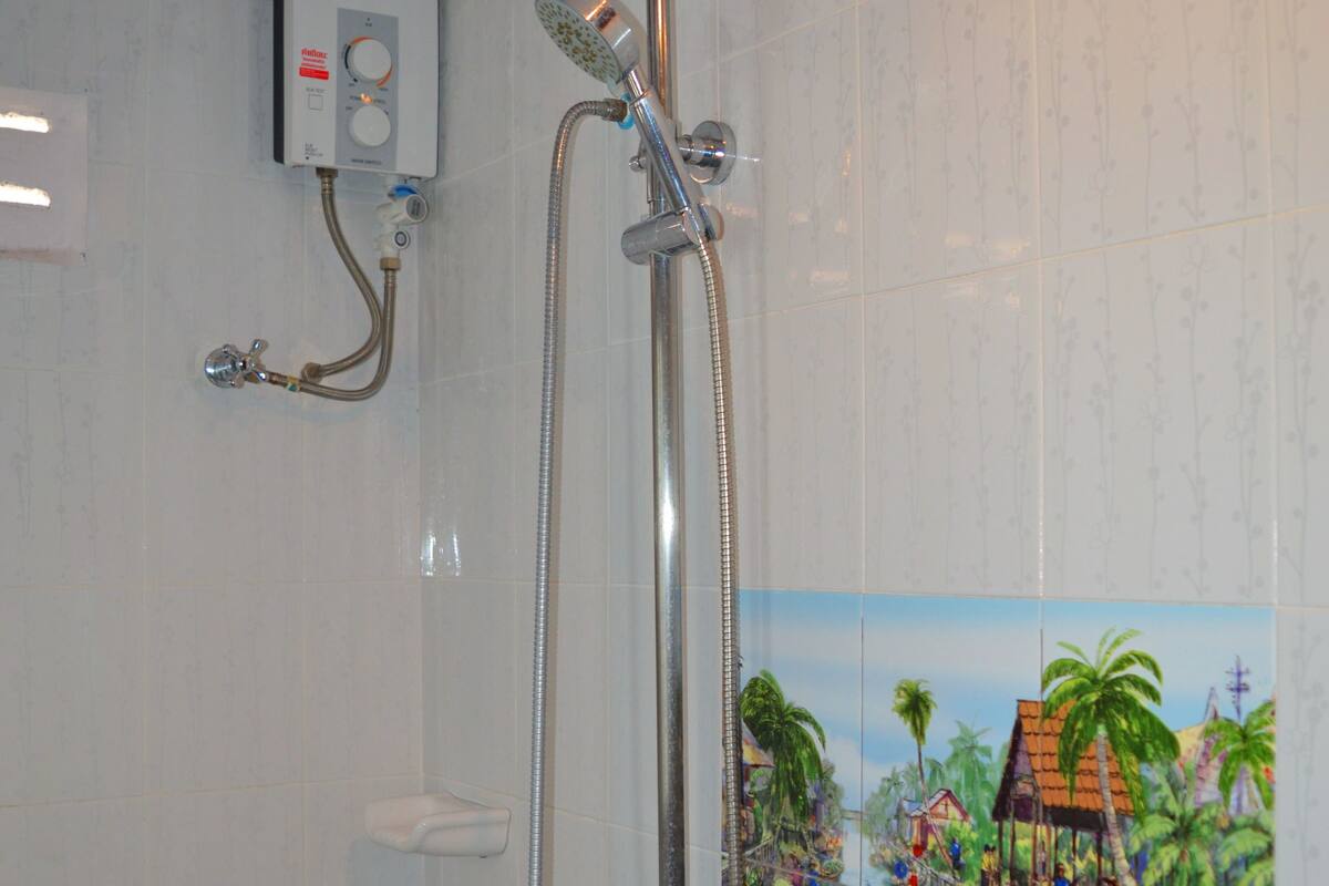 A shower with a rain showerhead and a handheld showerhead, a control panel, and a tiled wall with a tropical mural.