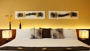 Habitación de hotel con una cama grande, dos cuadros colgados en la pared, una mesita de noche con una lámpara y un jarrón con flores.