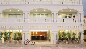 Un hotel de varios pisos con una entrada imponente, plantas en macetas y una bicicleta estacionada afuera.