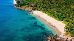 A coastal landscape with a sandy beach, clear turquoise waters, and lush green hills.