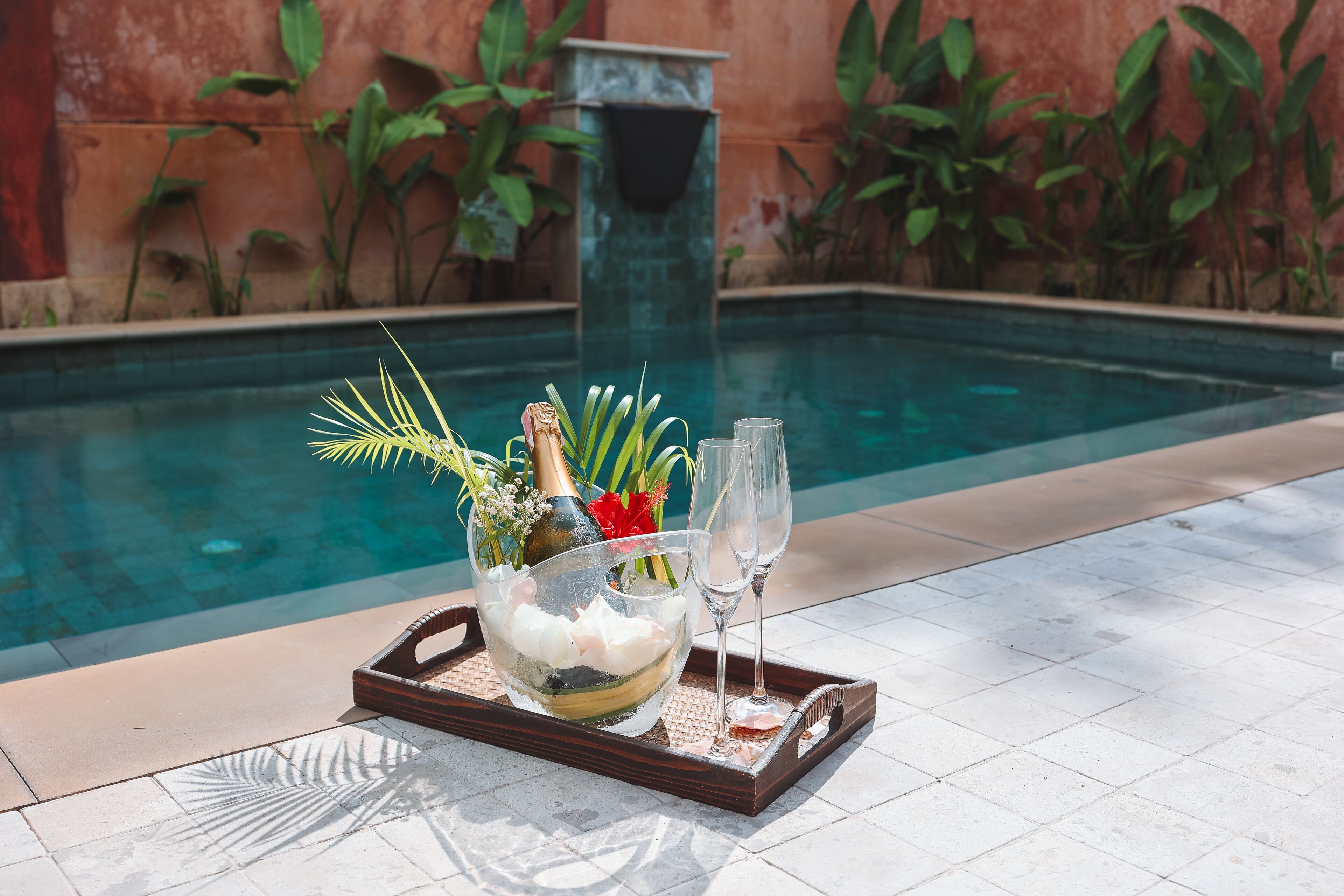 A tray with a chilled drink, a bottle, and a glass on a tiled poolside area.
