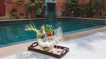 A tray with a chilled drink, a bottle, and a glass on a tiled poolside area.