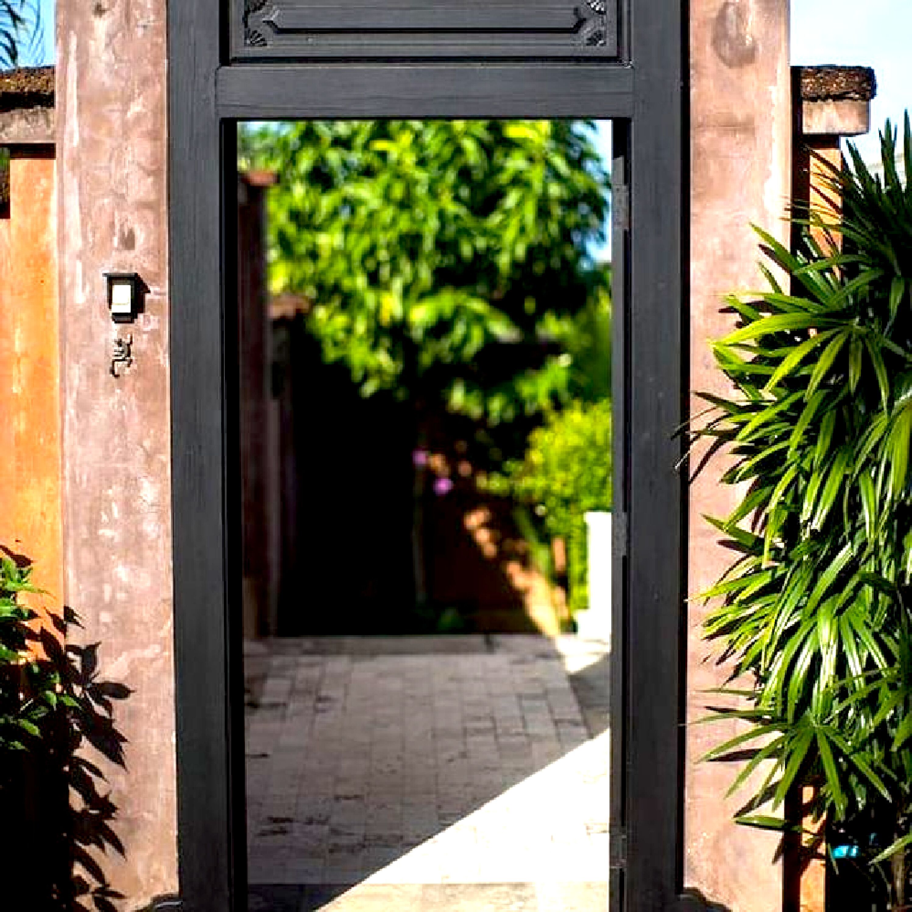 An entrance with a dark frame, a pathway leading through, and greenery on either side.