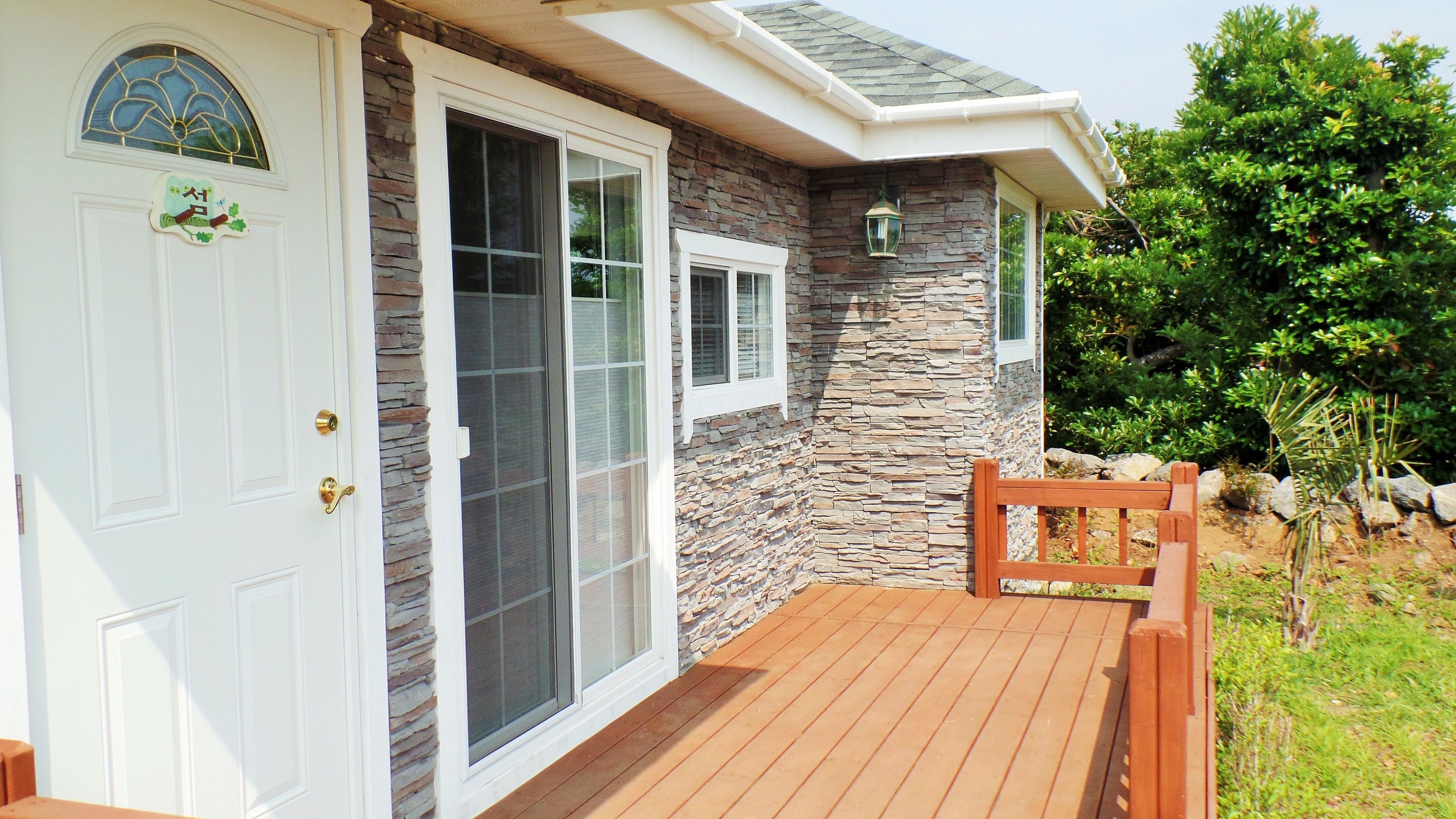 A house with a stone exterior, a wooden deck, and a white door with a glass panel.