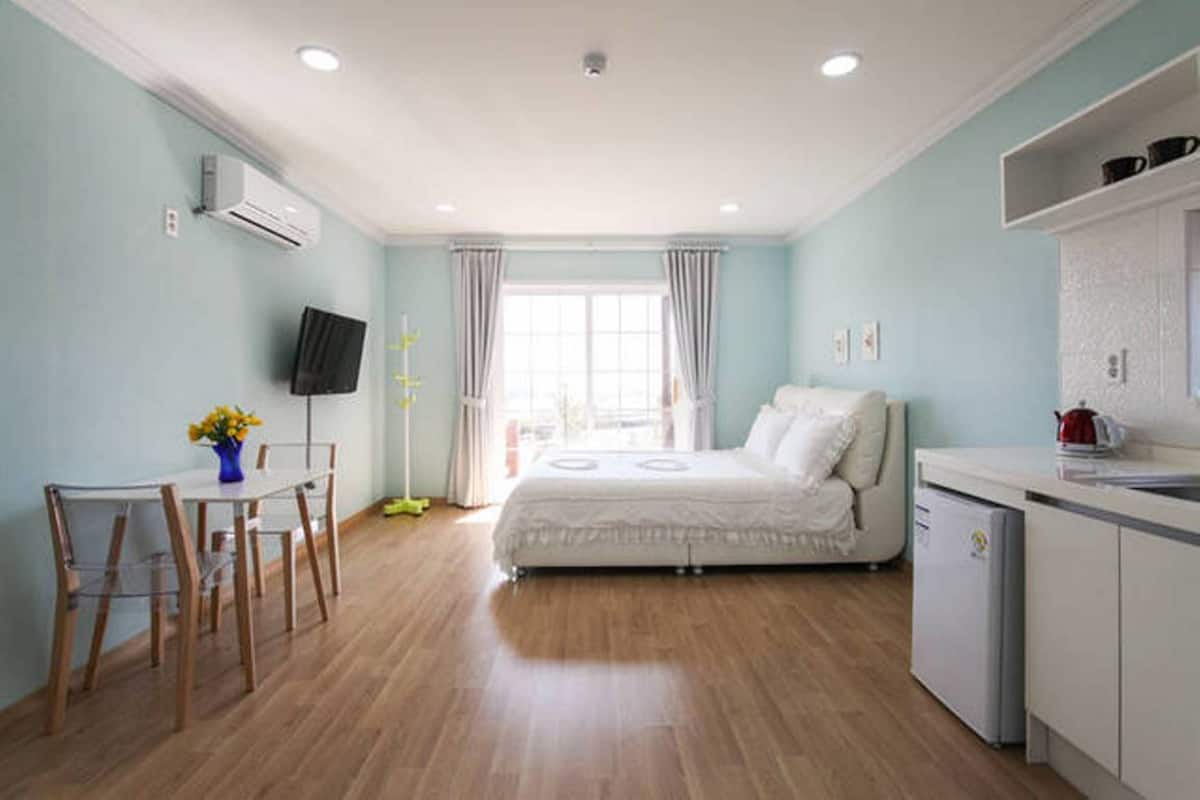 A room with a bed, a desk, a chair, a television, and a window with curtains.