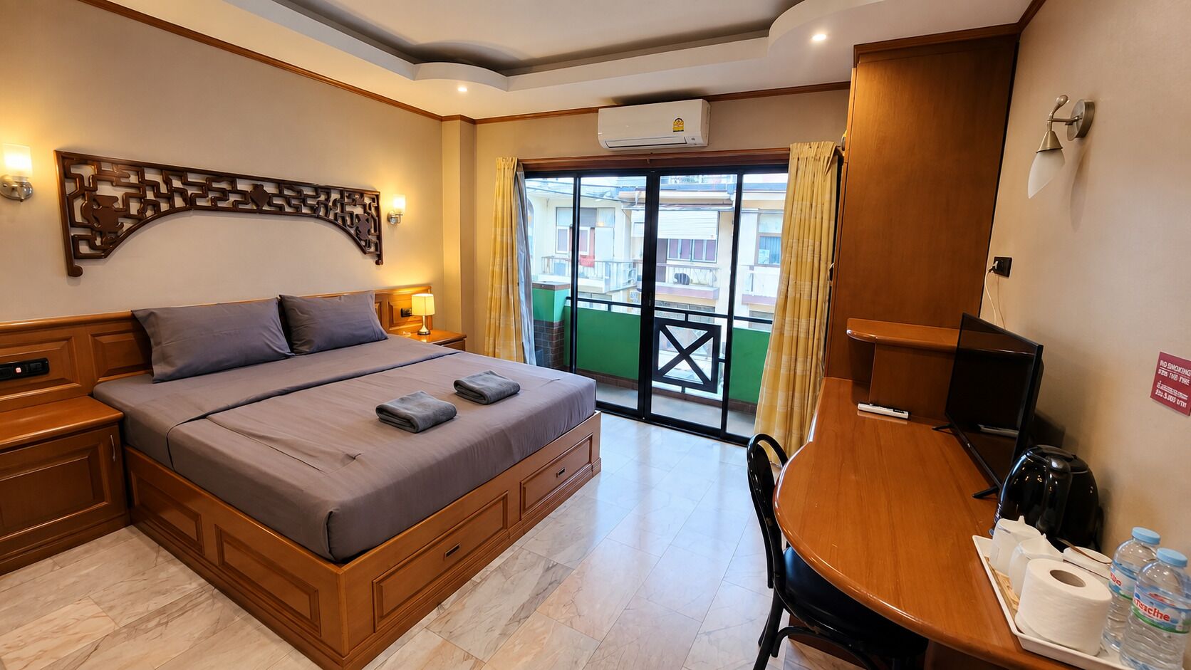 A hotel room with a bed, a desk, a chair, a television, and a balcony with a view.