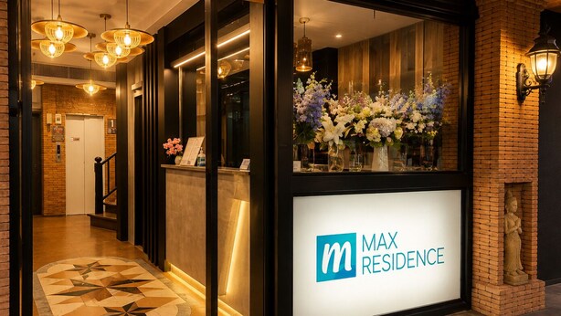 A hotel reception area with a modern design, featuring a reception desk, a staircase, and a decorative flower arrangement. - Max Residence (Pattaya)