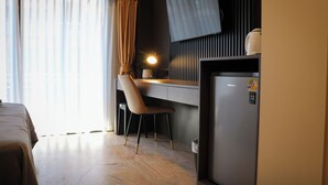 A hotel room with a bed, a desk with a chair, a refrigerator, and a window with curtains. - Max Residence (Pattaya)