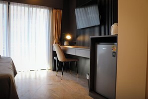Une chambre d’hôtel comprenant un lit, un bureau avec une chaise, un réfrigérateur et une fenêtre avec des rideaux.