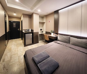 A hotel room with a bed, a desk, a small kitchenette, and a bathroom. - Max Residence (Pattaya)