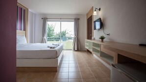 A hotel room with a bed, a TV mounted on the wall, a small plant on the side table, and a balcony with a view of greenery. - The Greenery Hotel (Krabi)