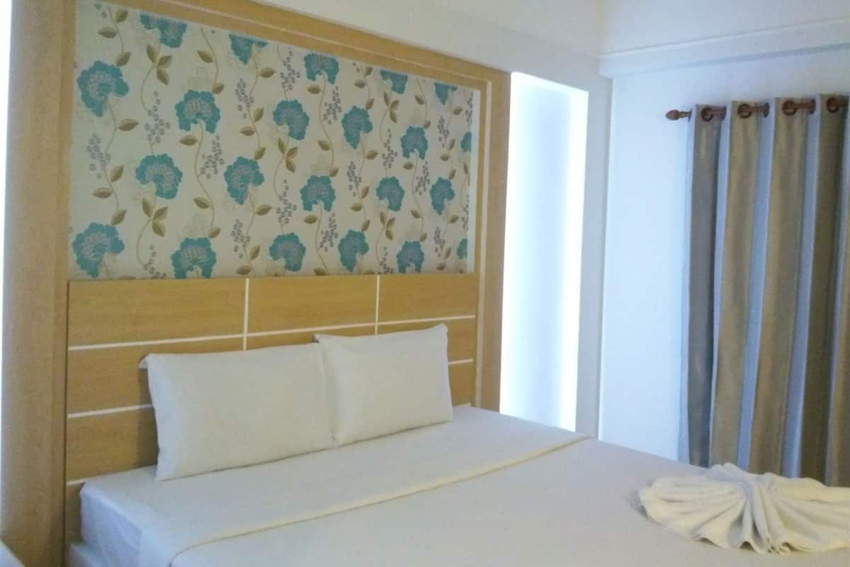 A hotel room with a bed, a headboard with floral wallpaper, and curtains.