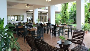 A spacious indoor dining area with multiple tables and chairs, surrounded by potted plants and a view of the outdoor garden. - The Greenery Hotel (Krabi)