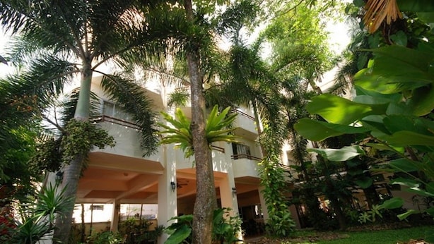 A multi-story building with a covered outdoor area surrounded by lush greenery, including palm trees and large-leafed plants. - The Greenery Hotel (Krabi)