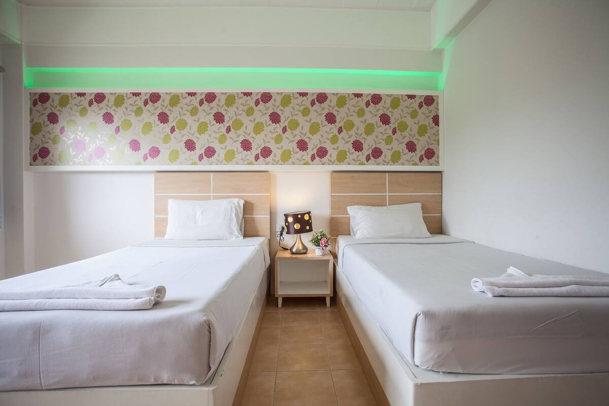 A hotel room with two beds, a nightstand with a lamp, and a floral-patterned headboard.
