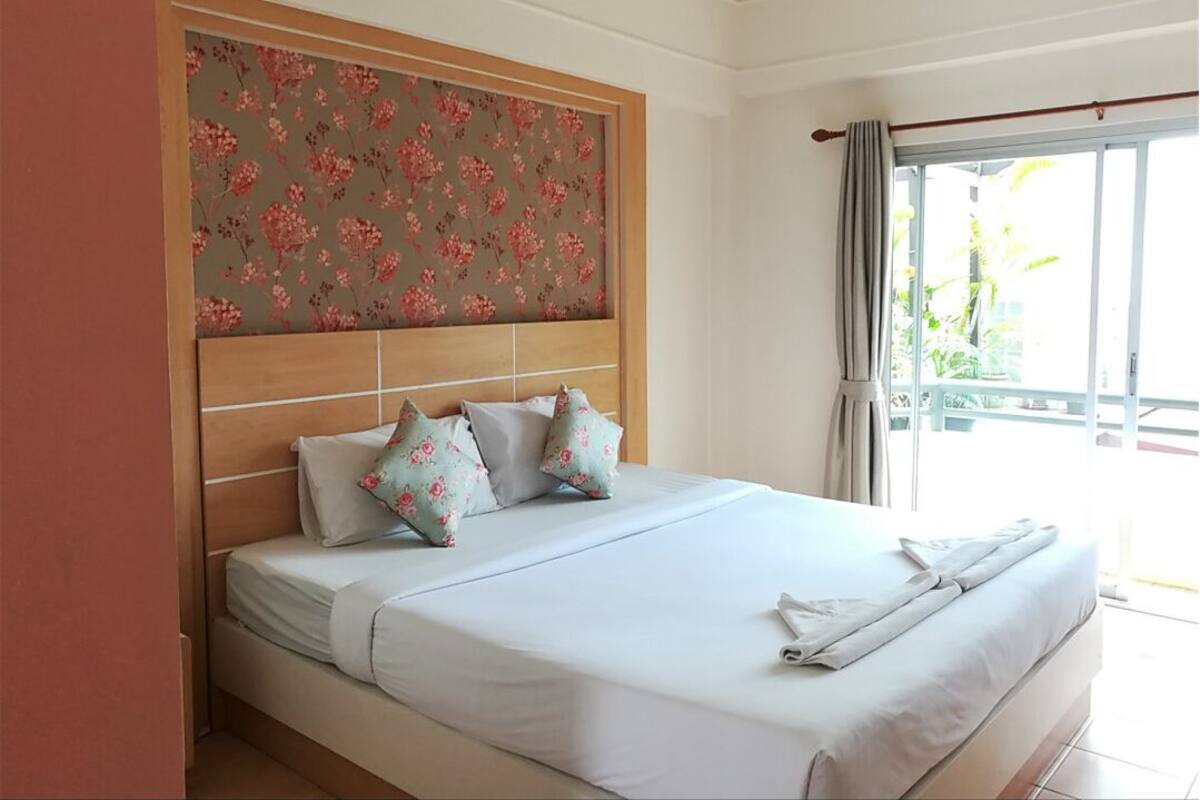 A hotel room with a large bed, a wooden headboard, and a balcony with a view.