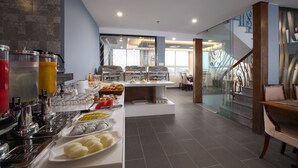 Ein modernes Frühstücksbuffet mit verschiedenen Speisen und Getränken, eine Treppe mit Glastrennwand und Blick ins Innenraum.