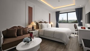 Ein modernes Hotelzimmer mit einem großen Bett, einer Couch, einem Schreibtisch und Blick auf die Stadt.