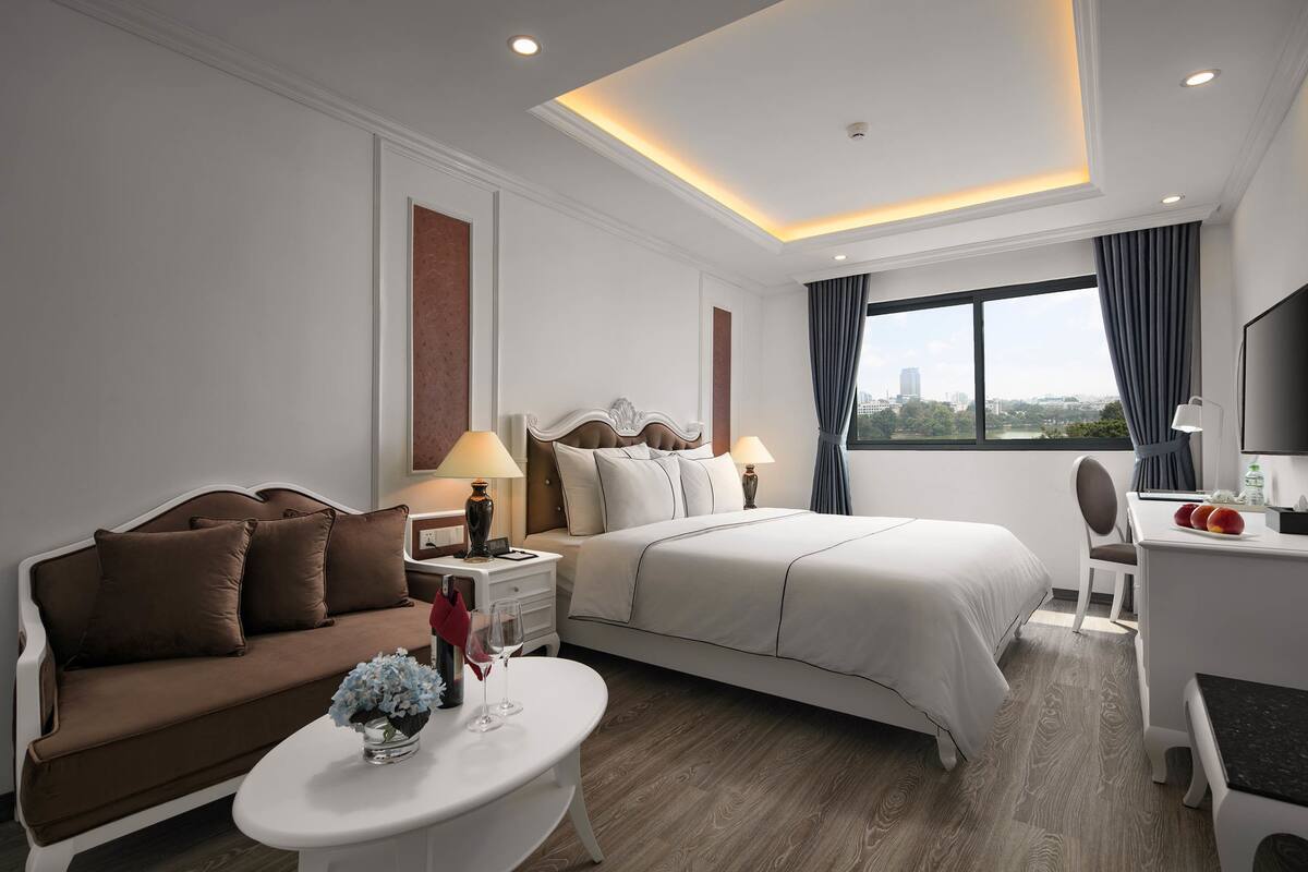 A modern hotel room with a large bed, a sofa, a desk, and a view of the city.