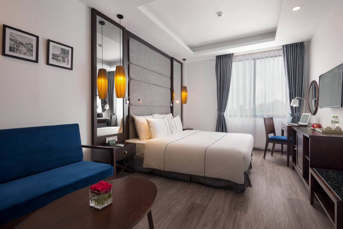 A hotel room with a bed, a blue sofa, a desk with a laptop, and a TV.