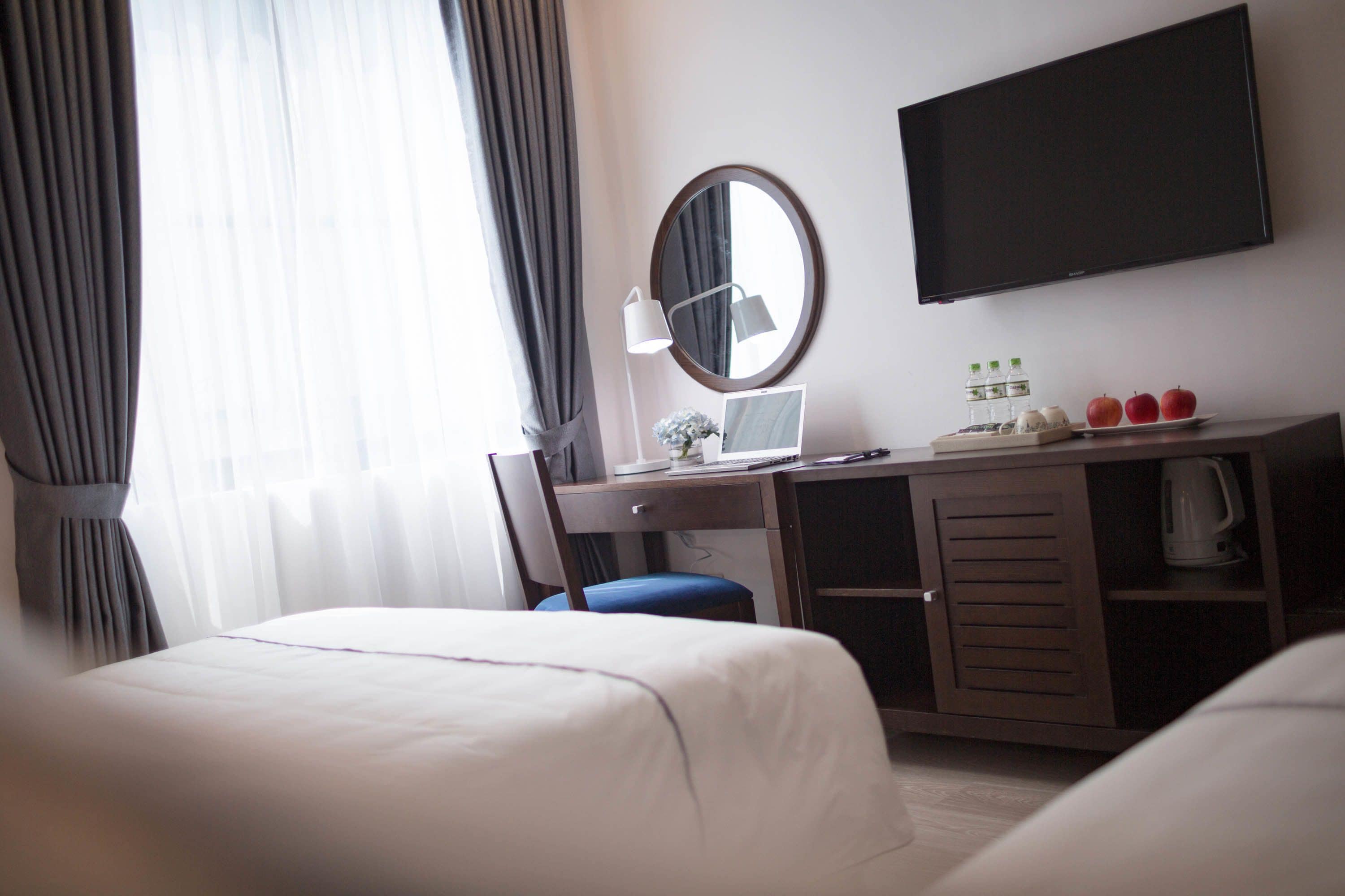 Habitación de hotel con cama, escritorio con computadora, televisión y pequeña área de kitchenette.