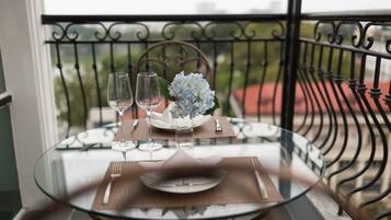 A glass table set with a plate, two wine glasses, and a vase of flowers on a balcony with a wrought iron railing.