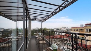 Ein Balkon mit Tischen, Stühlen und einer Glasreling, mit Blick auf die Stadt.