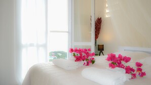 Een hotelkamer met een groot bed, witte lakens en roze bloemen.