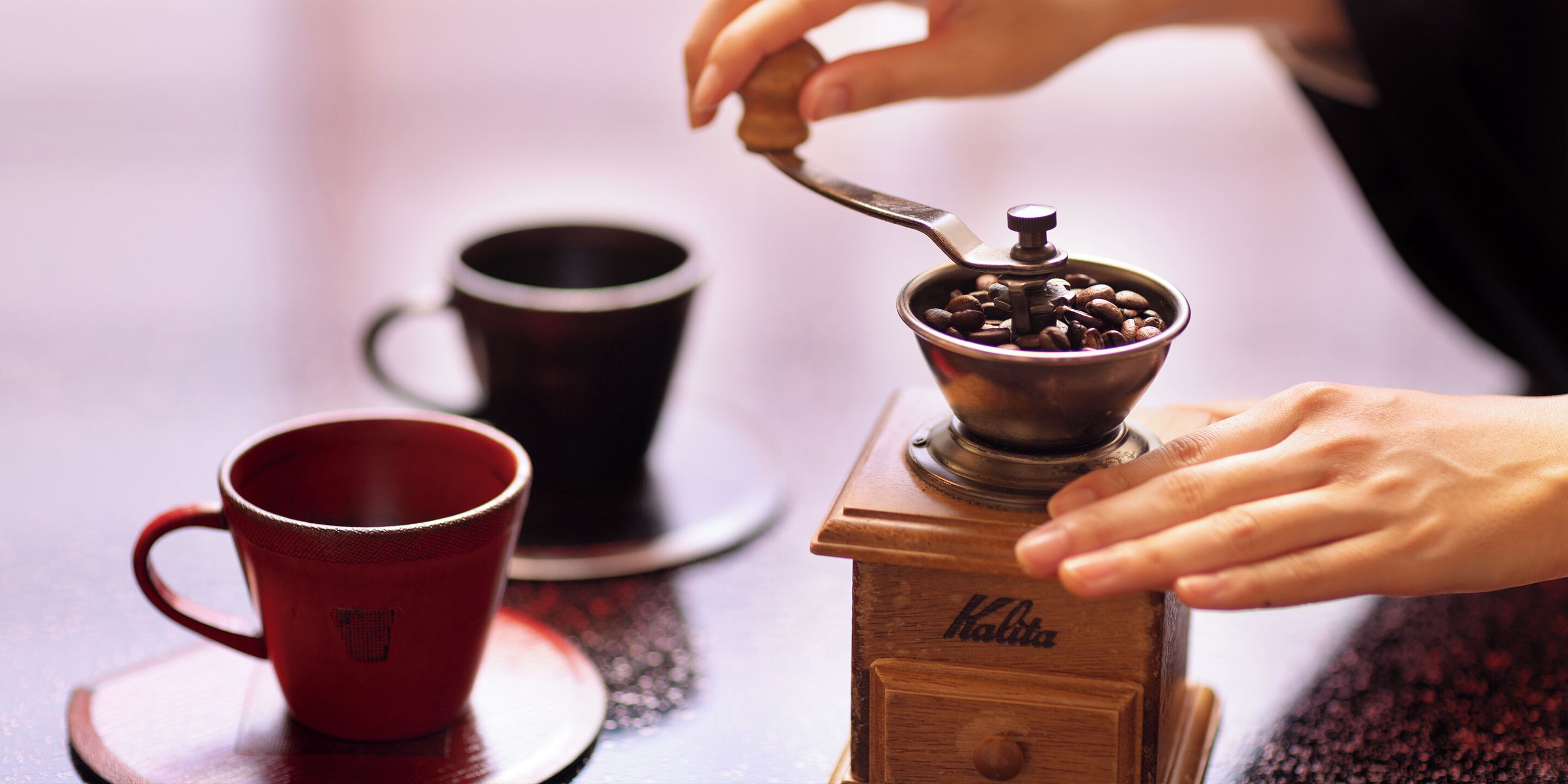 A coffee grinder with a red cup and a black cup on a wooden table.