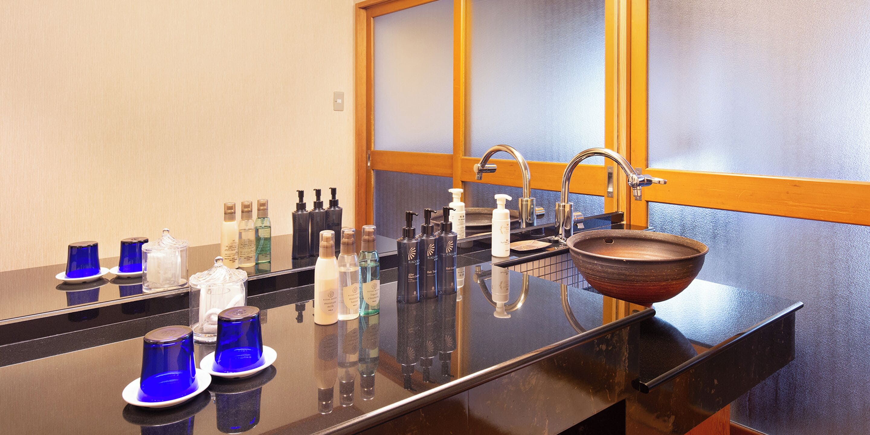 A bathroom with a black countertop, a wooden bowl sink, and various toiletries.