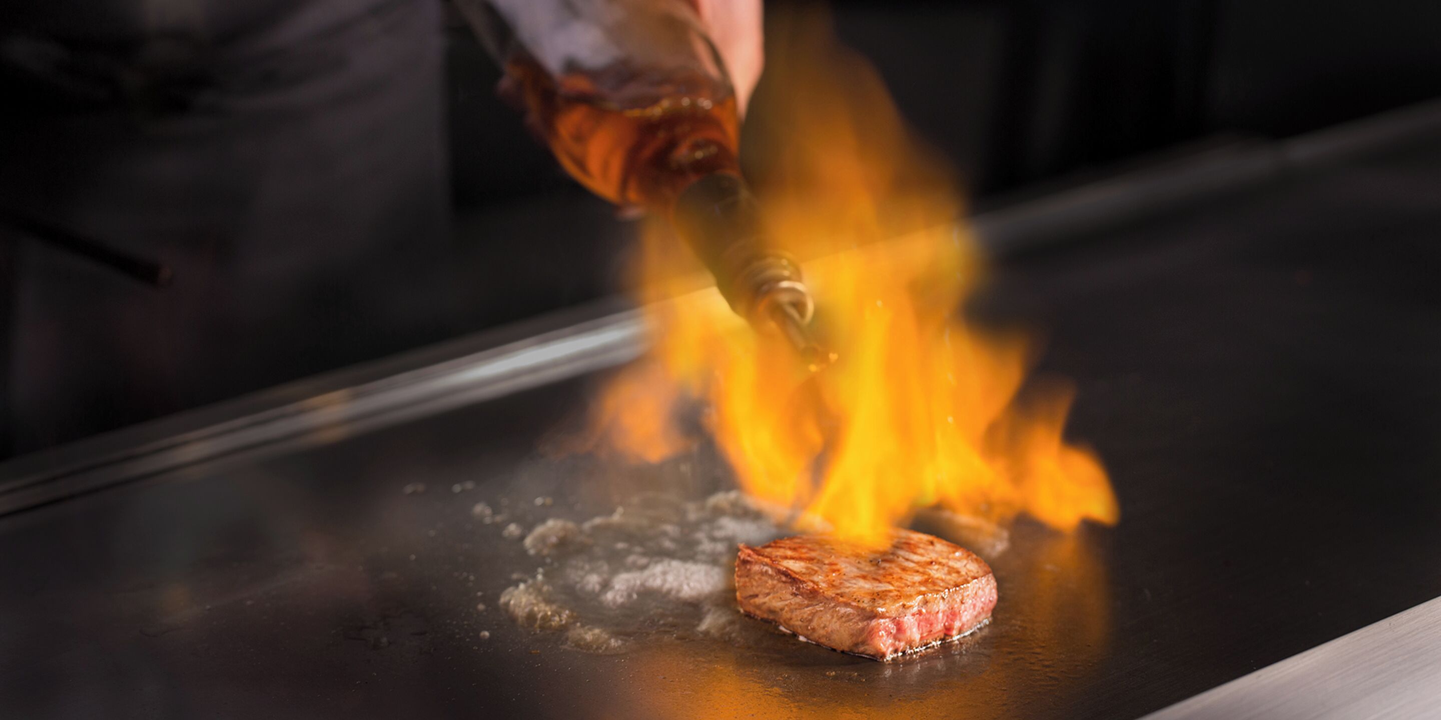 A steak being grilled on a flat surface with flames.