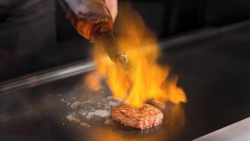 A steak being grilled on a flat surface with flames.
