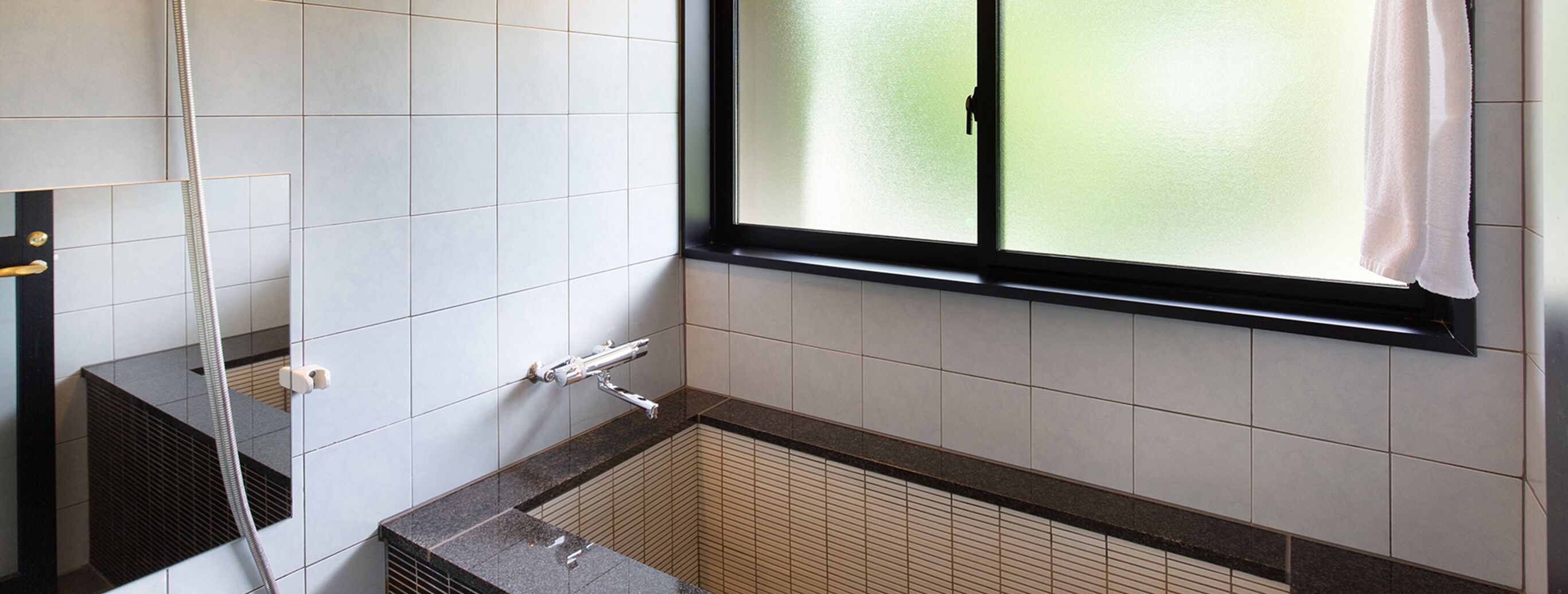 A bathroom with a shower, a window with a curtain, and tiled walls.