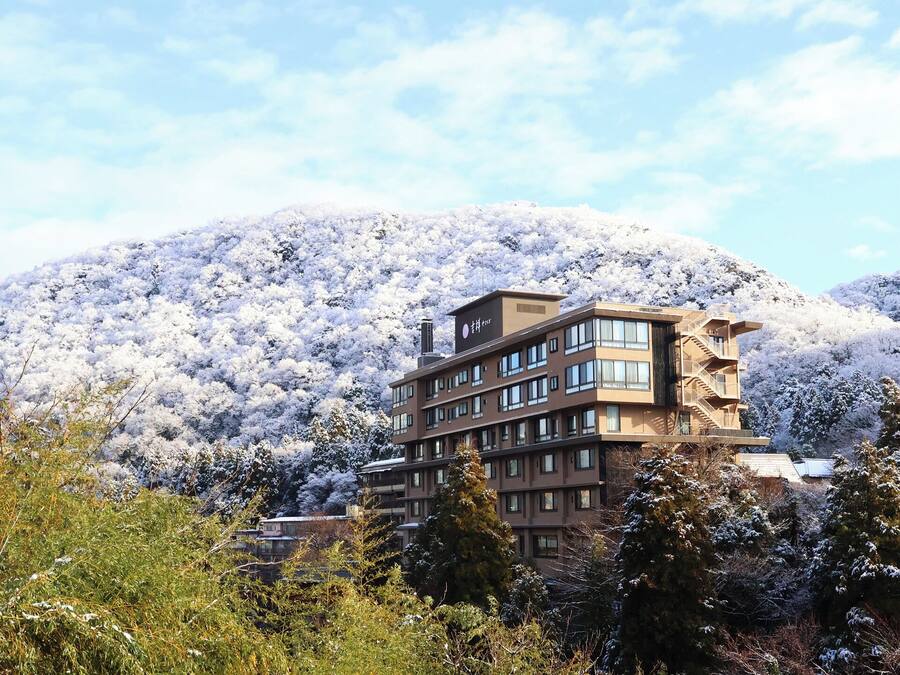 Ein mehrstöckiges Hotel mit modernem architektonischem Design, umgeben von schneebedeckten Bäumen und Hügeln.
