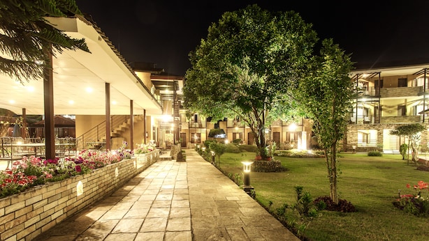 A well-lit pathway leading to a building with multiple balconies and a garden area with flowers and a lawn. - The Lakeside Retreat Pokhara by IME Hospitality (Pokhara)