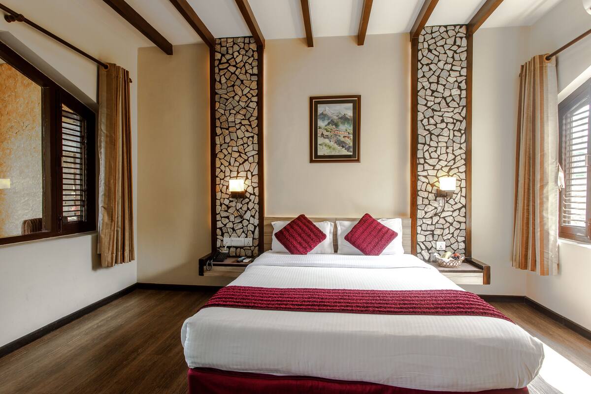 A hotel room with a large bed, wooden beams, stone wall panels, and a framed picture on the wall.