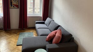 A living room with a grey sofa, red curtains, a framed picture on the wall, and a window with a view of buildings. - GoVienna Homelike City Apartment (Vienna)