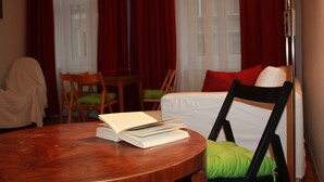 A hotel room with a round wooden table, a bed with white bedding and red pillows, a green chair, and a lamp. - GoVienna Homelike City Apartment (Vienna)