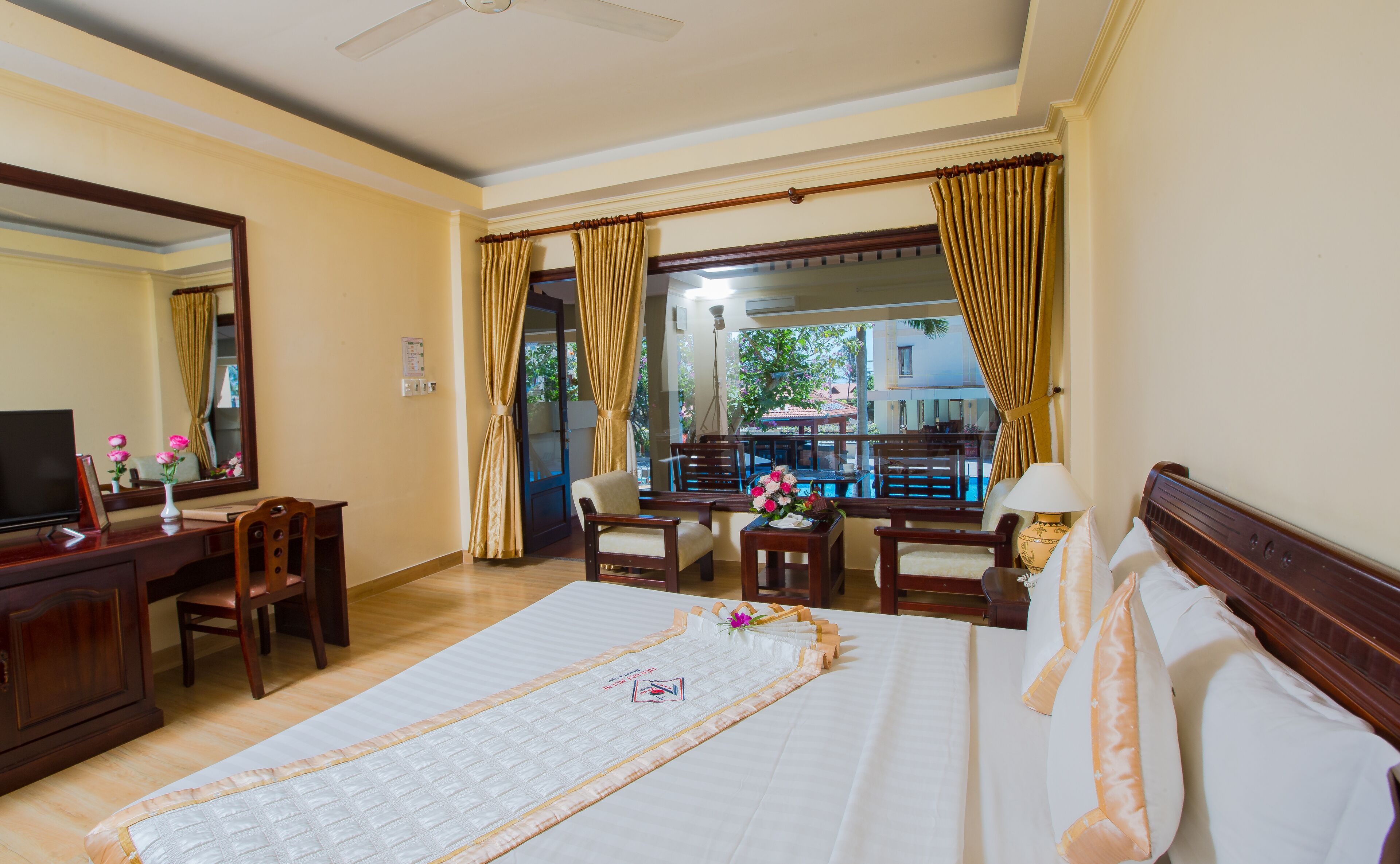 Habitación de hotel con cama, escritorio con televisor, silla, lámpara y vistas al exterior.