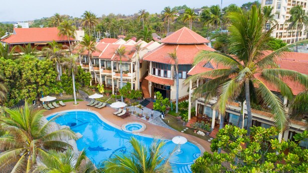 Un resort con piscina, palmeras y edificios con techos rojos.