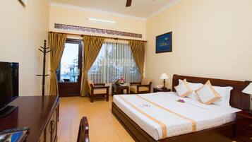 A hotel room with a large bed, a desk with a TV, a chair, a desk lamp, and a ceiling fan.