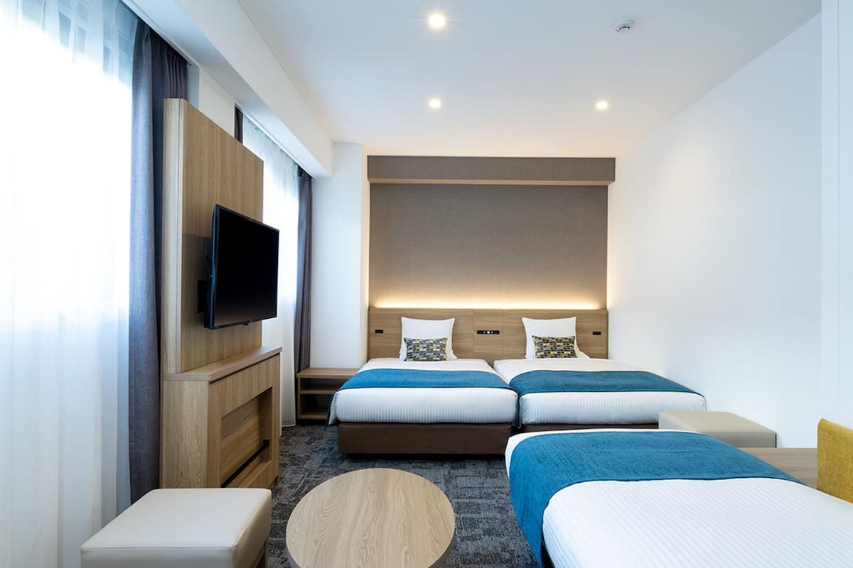 Quarto de hotel com duas camas, televisão, uma mesinha e um sofá.