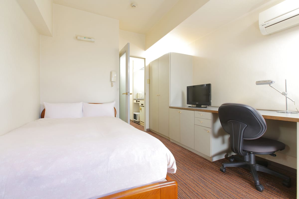 Quarto de hotel com cama, escrivaninha com computador, cadeira e televisão.