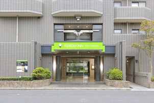 L'entrée du FLEXSTAY INN à Shin-Urayasu se distingue par son design moderne, sa façade en verre transparent et un jardinier en pierre agrémenté de plantes vertes.
