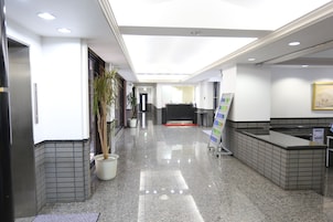 A clean, well-lit lobby with a reception desk, potted plants, and a tiled floor.
